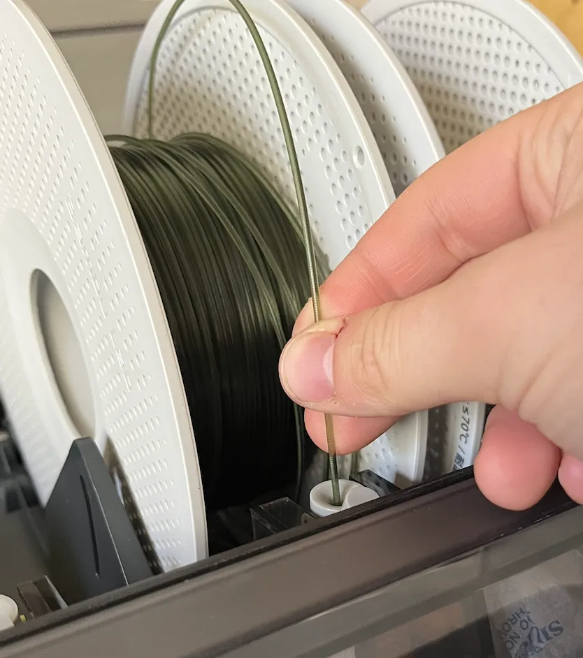A hand pushing dark green filament into an AMS filament inlet