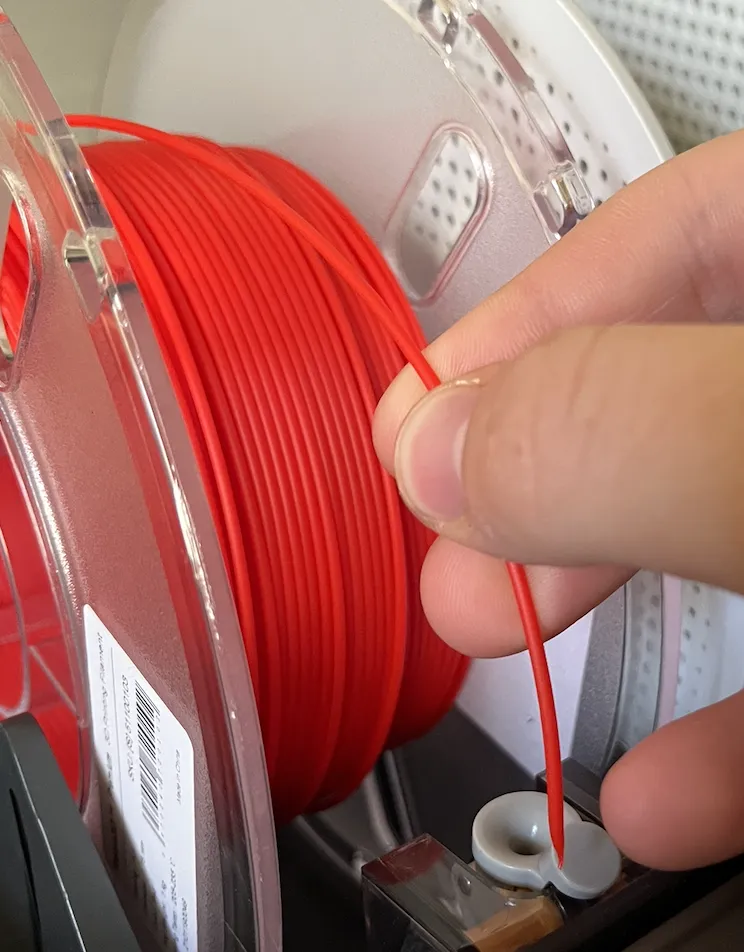 A hand pushing red filament into an AMS filament inlet