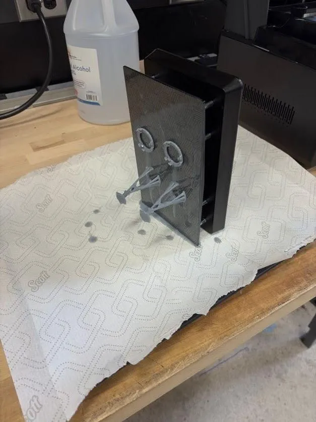 The build plate stood on its edge on a towel-lined baking sheet, still wet with grey resin