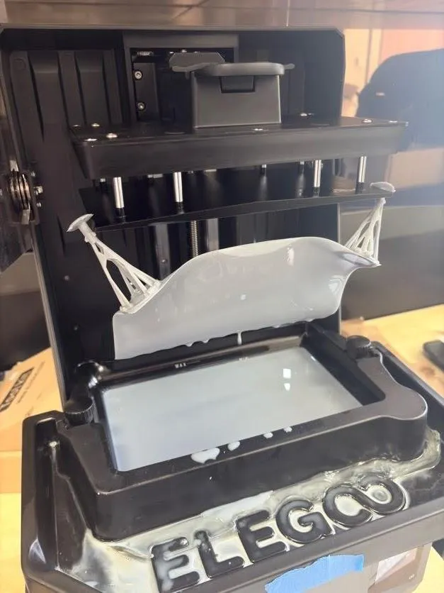 The cured resin sheet hanging between two stems hooked over the build plate above the tank