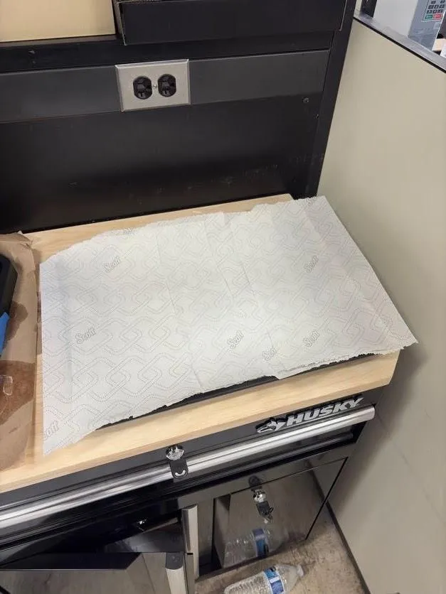 A baking sheet lined with shop towels on a bench next to the printer