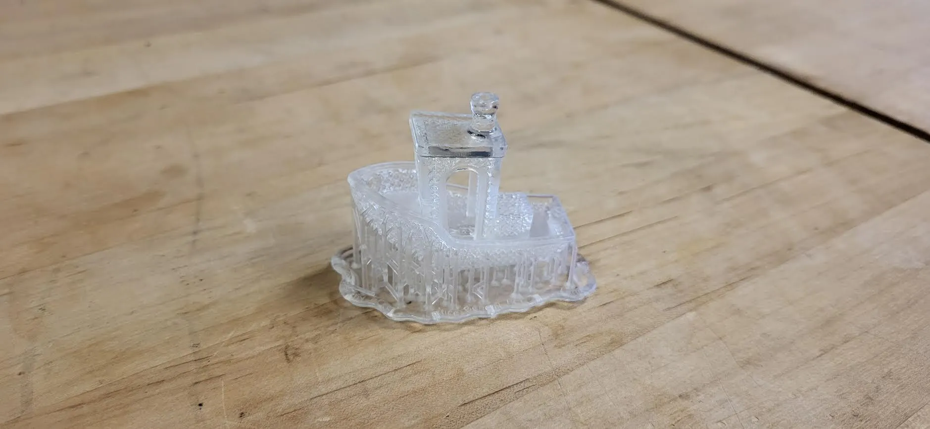 A finished clear resin lattice Benchy on a workbench, supports and raft still attached
