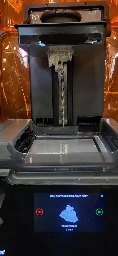 A finished print hanging from the build platform above the resin tank, dripping resin back into the tank