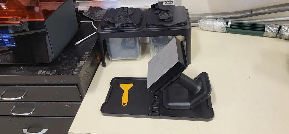 The Fab Lab's finishing station in use: gloves drying on two lidded buckets, and a build platform on its jig on the finishing tray with a yellow plastic scraper