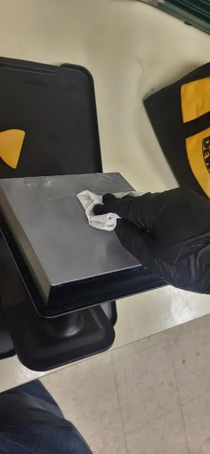 A gloved hand wiping resin off a build platform with a blue shop towel